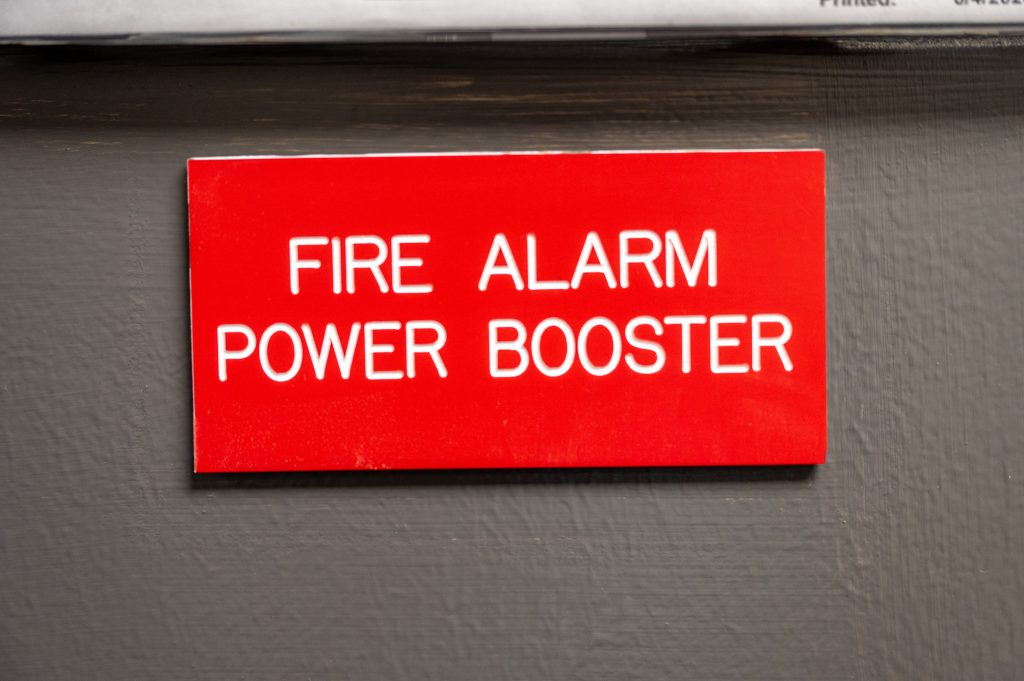 Engraved sign in red with "Fire Alarm Power Booster" text
